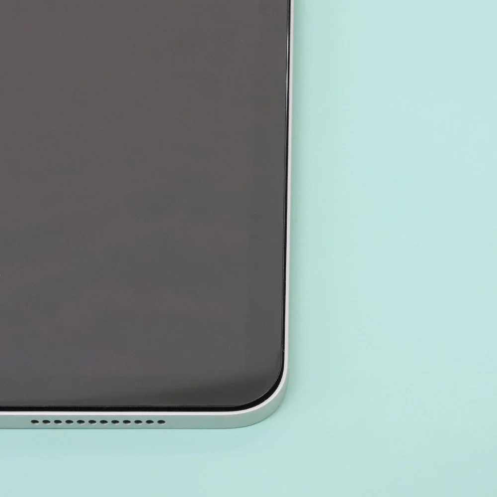 水色の背景に置かれた、画面がオフの状態のタブレットまたはスマートフォンの下部が写っています