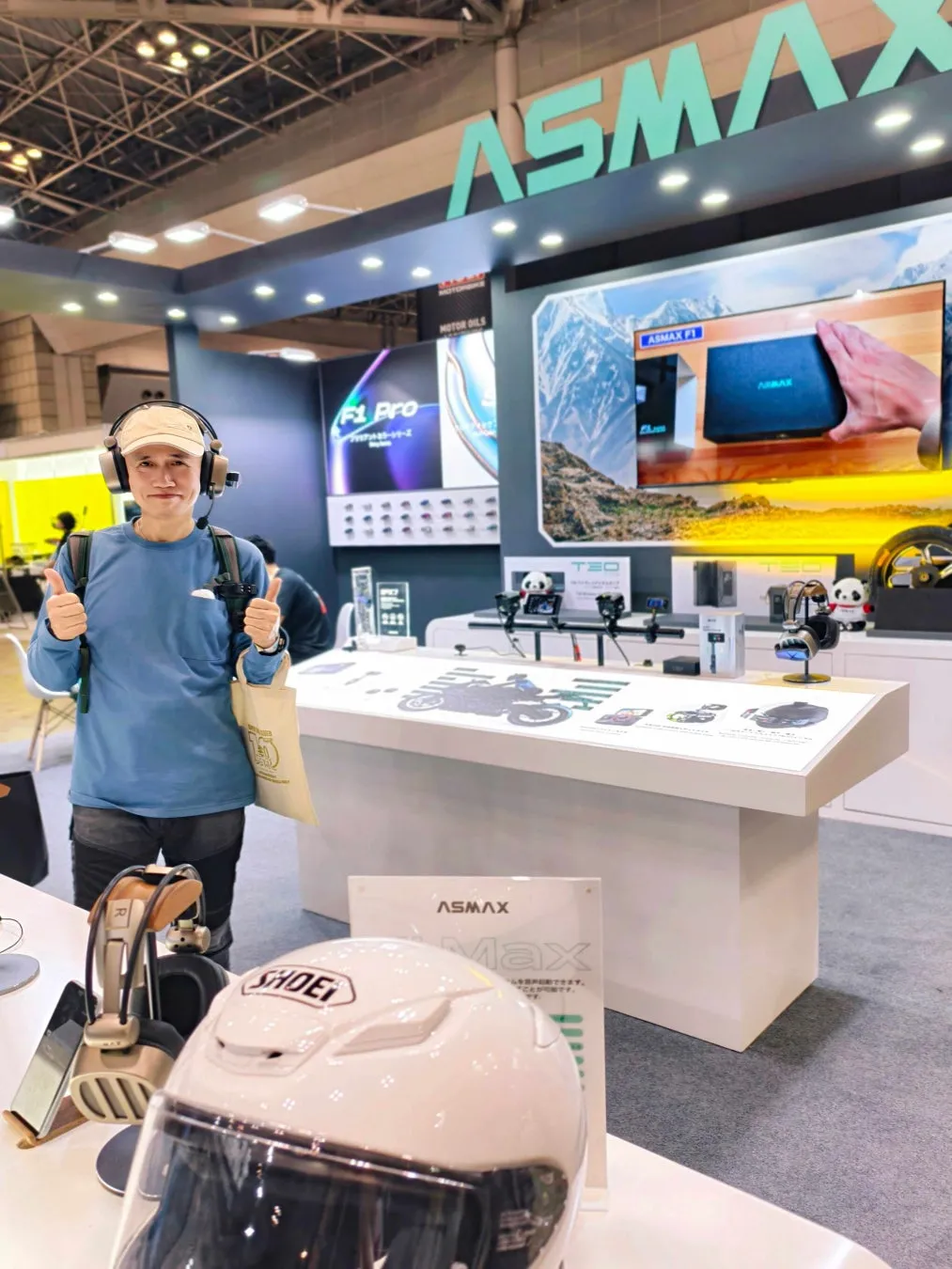 展示会で、ASMAXのブースでサムズアップをしている男性