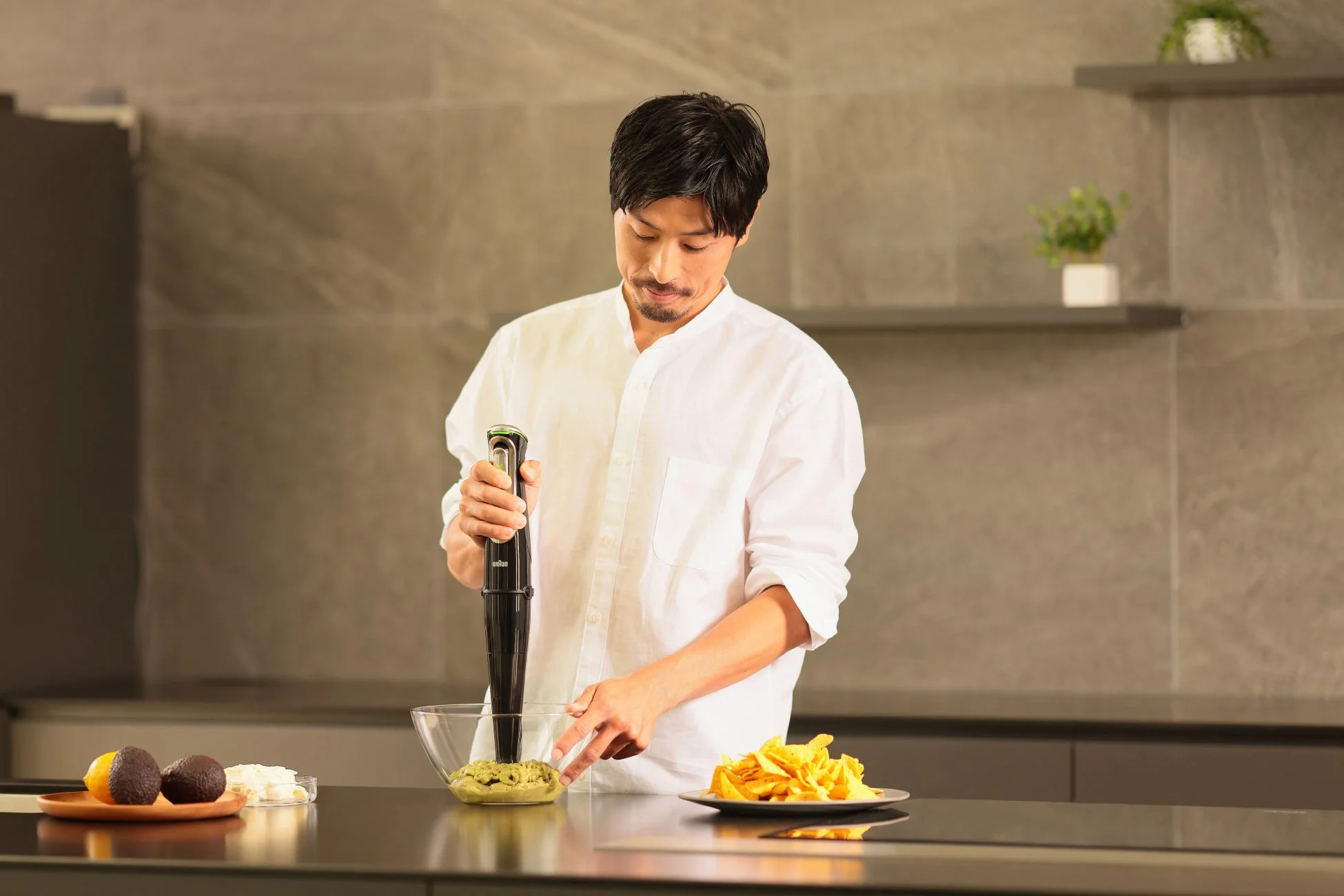 男性がハンドブレンダーでワカモレのようなものを混ぜている画像