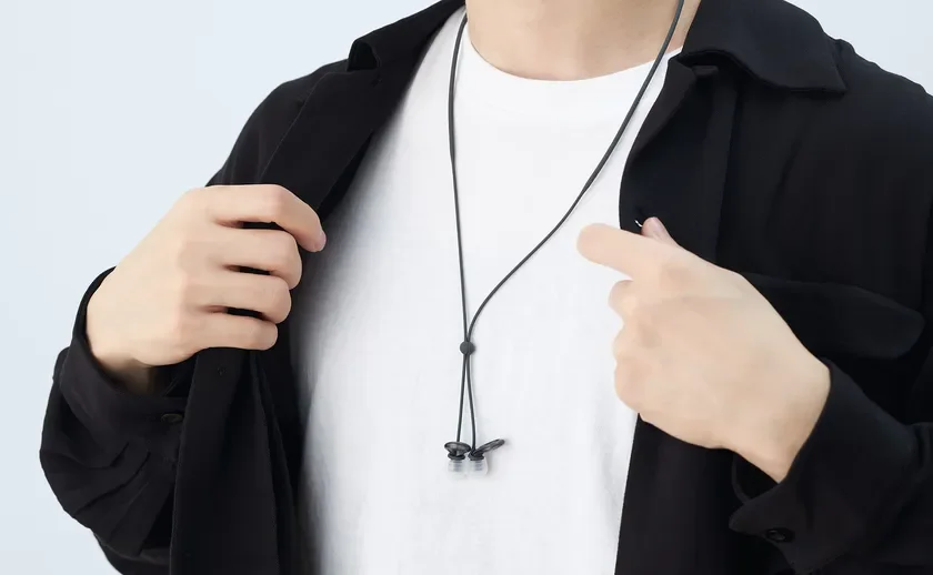 白いTシャツの上に黒いシャツを羽織った人物が、首にネックバンド型のイヤホンを着用している様子