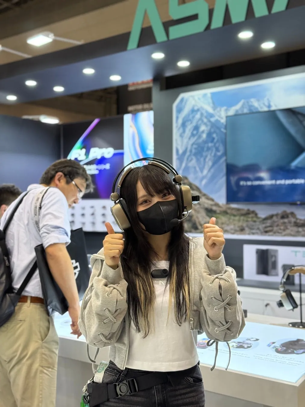 展示会でヘッドホンを着けた女性が親指を立てている様子