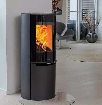 モダンなデザインの黒い薪ストーブが部屋の隅に設置されており、ガラス窓からは炎が力強く燃えているのが見えます