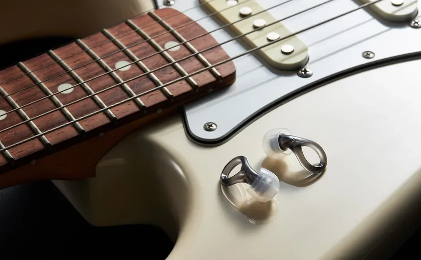 クリーム色のエレキギターのボディに、スタイリッシュなワイヤレスイヤホンが置かれているクローズアップ写真