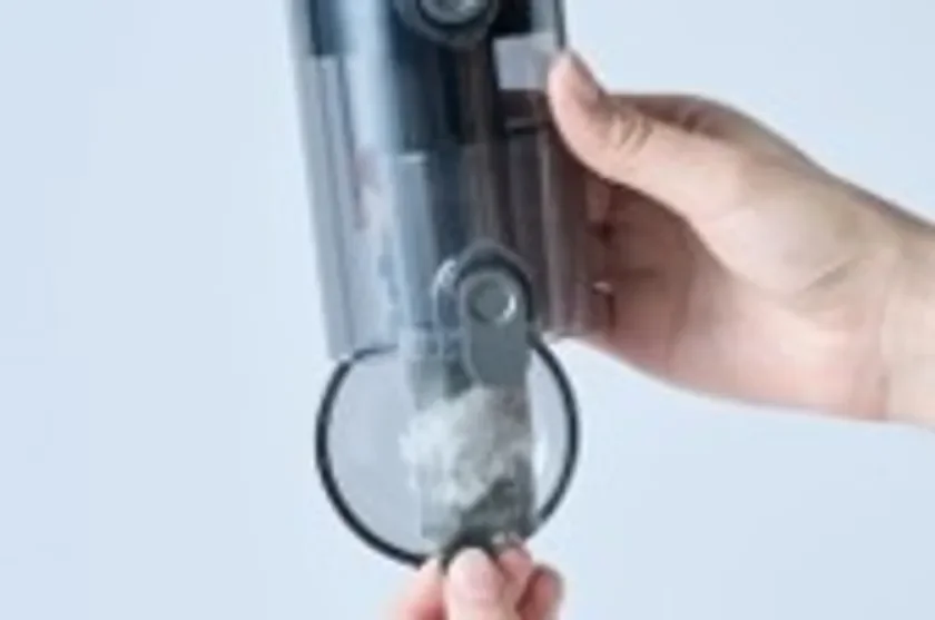掃除機のダストカップに溜まったホコリやゴミを、手が持って排出している様子