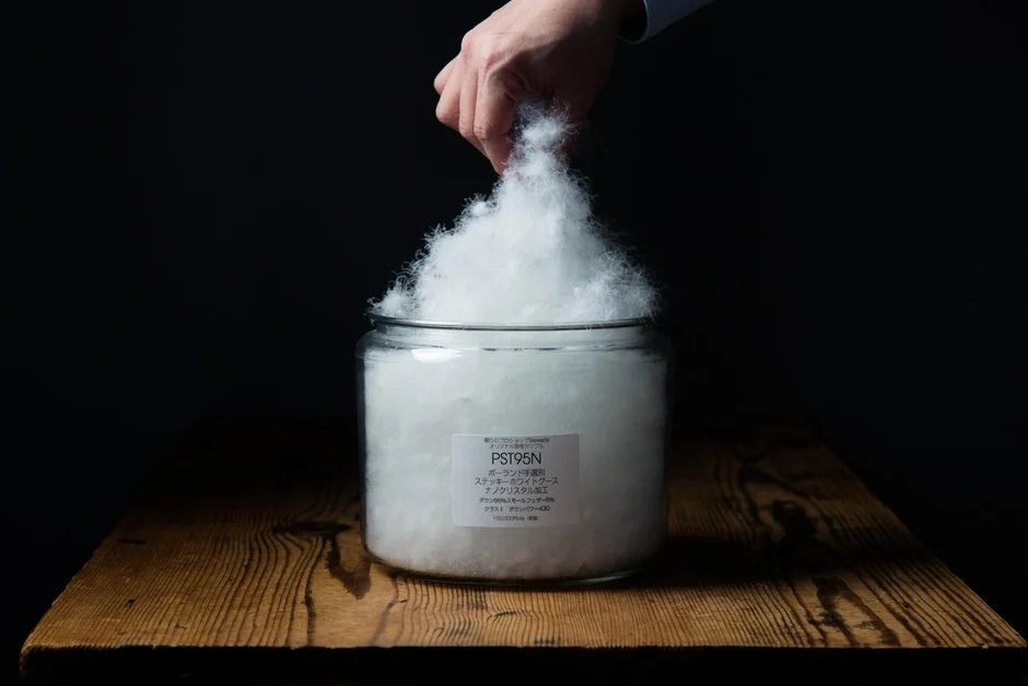 ガラス瓶から白いふわふわの羽毛を優しく取り出す手