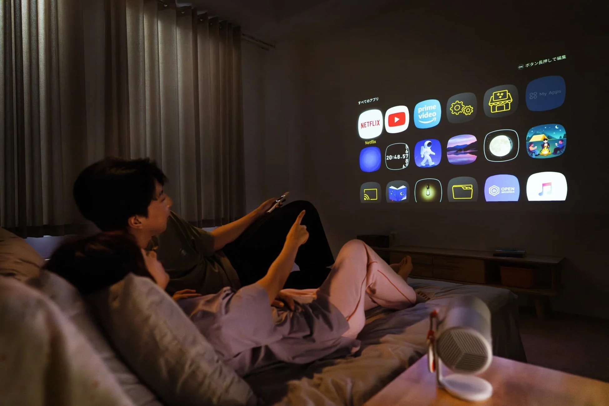 寝室でアプリ画面をプロジェクターで見るカップル