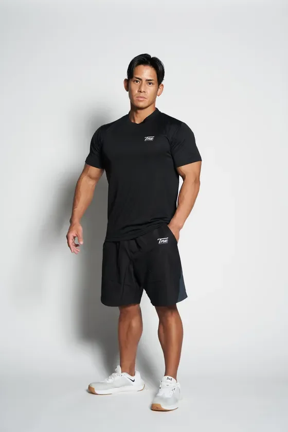 筋肉質な男性が黒いスポーツTシャツとハーフパンツを着用し、自信に満ちたポーズ