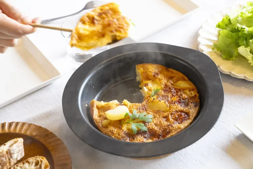 熱々のスパニッシュオムレツが黒いフライパンに盛られ、一部が取り分けられている食卓の様子