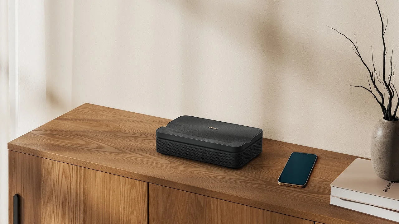 木製のキャビネットの上に、黒いプロジェクター、スマートフォン、そして枝物の入った花瓶が置かれた、ミニマリストでモダンなインテリア