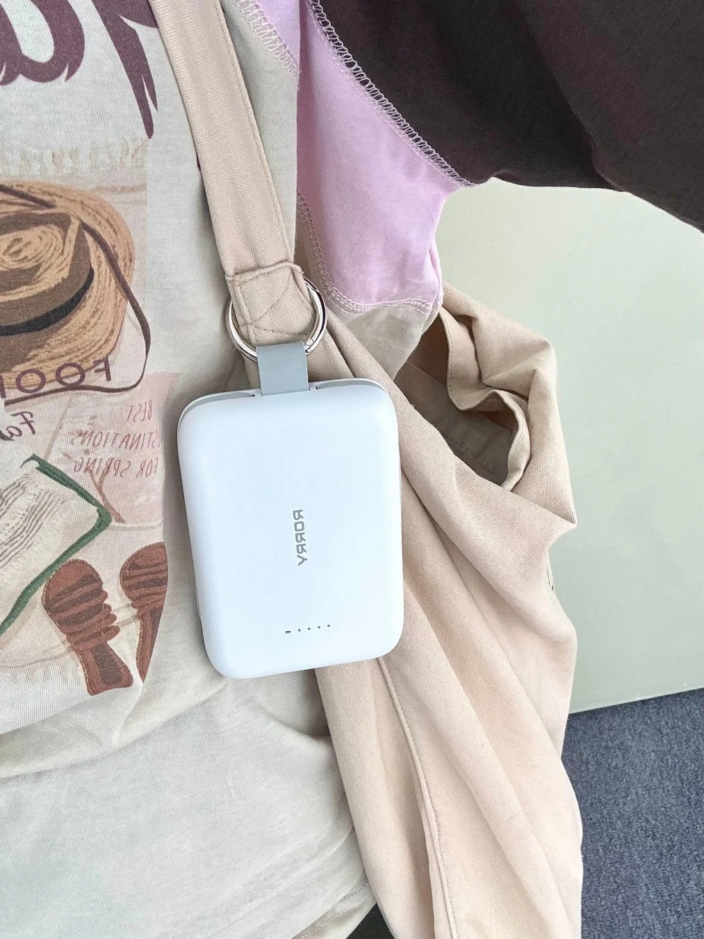 ベージュのトートバッグに白いポータブル充電器が吊り下げられている