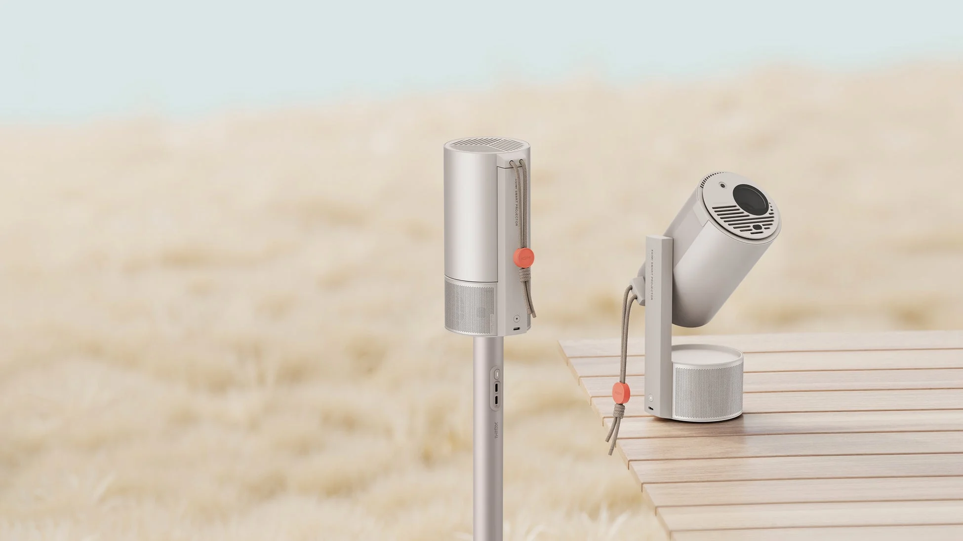 XGIMIのスマートプロジェクターが2台、屋外の砂浜のような背景と木製のテーブルに配置されています。洗練されたデザインの製品が、自然な環境に溶け込んでいる様子が伺えます。