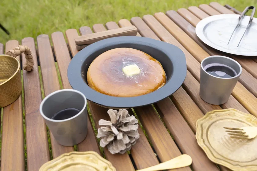 アウトドアの木製テーブルに置かれた大きなパンケーキと飲み物の写真