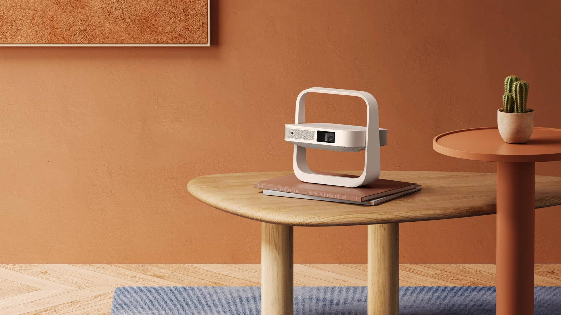 テラコッタ色の壁を背景に、木製のテーブルの上に置かれたスタイリッシュな白いプロジェクターが特徴的なモダンなインテリアシーンです。隣にはサボテンの鉢植えが飾られています。