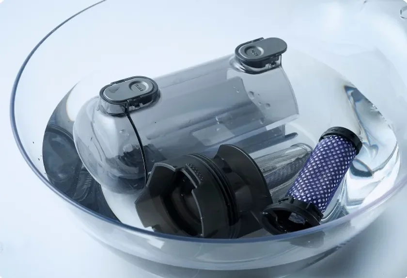 掃除機のダストカップとフィルターが透明なボウルに入った水に浸されており、部品を水洗いして清掃している様子