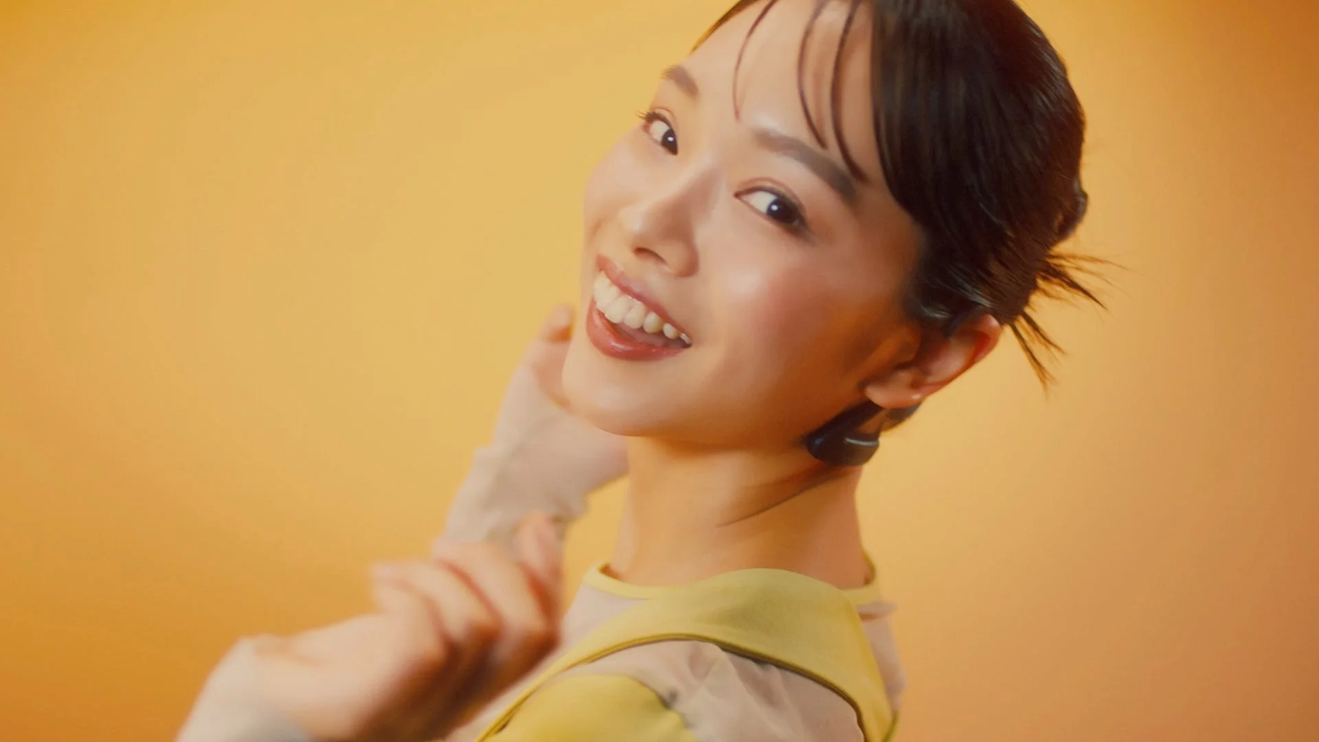 明るく微笑む若い日本人女性のポートレート。耳にイヤホンを装着。