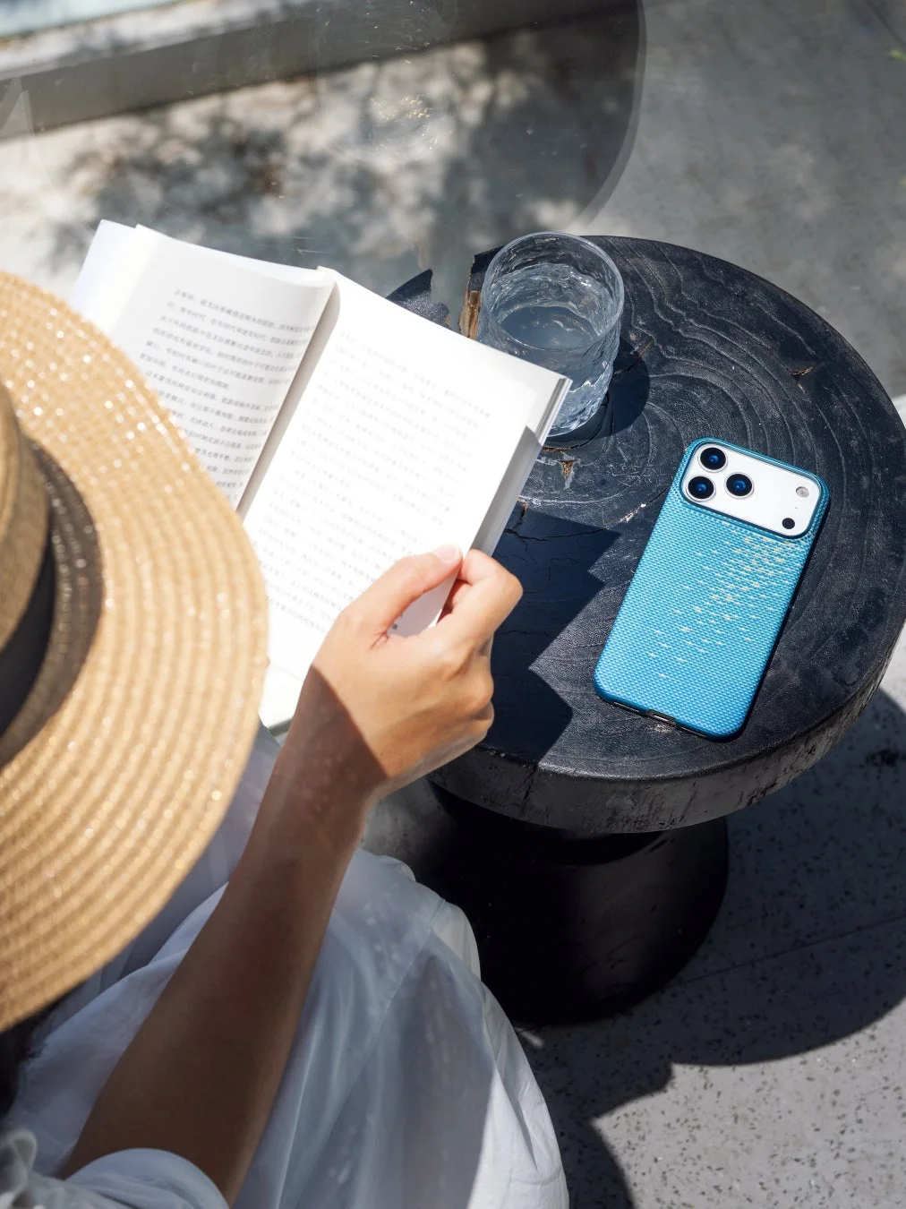 水辺で本を読む人のそばにあるスマホ