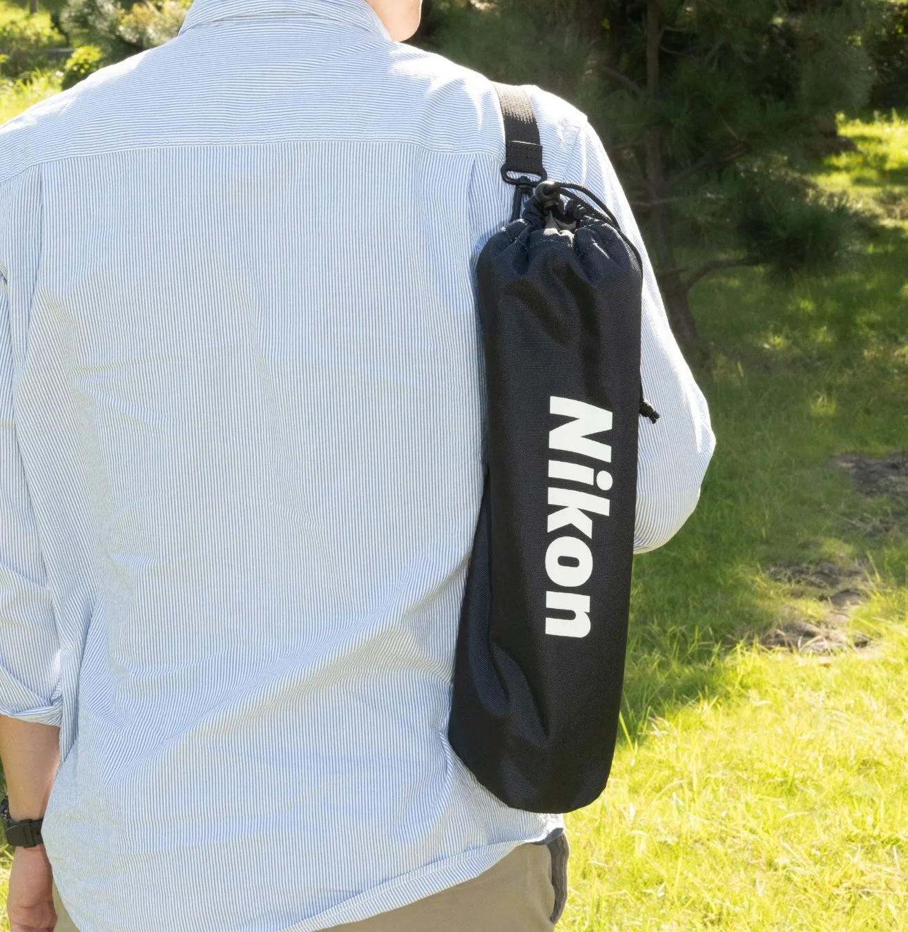 男性がNikonロゴ入りバッグを肩にかけて歩く後ろ姿