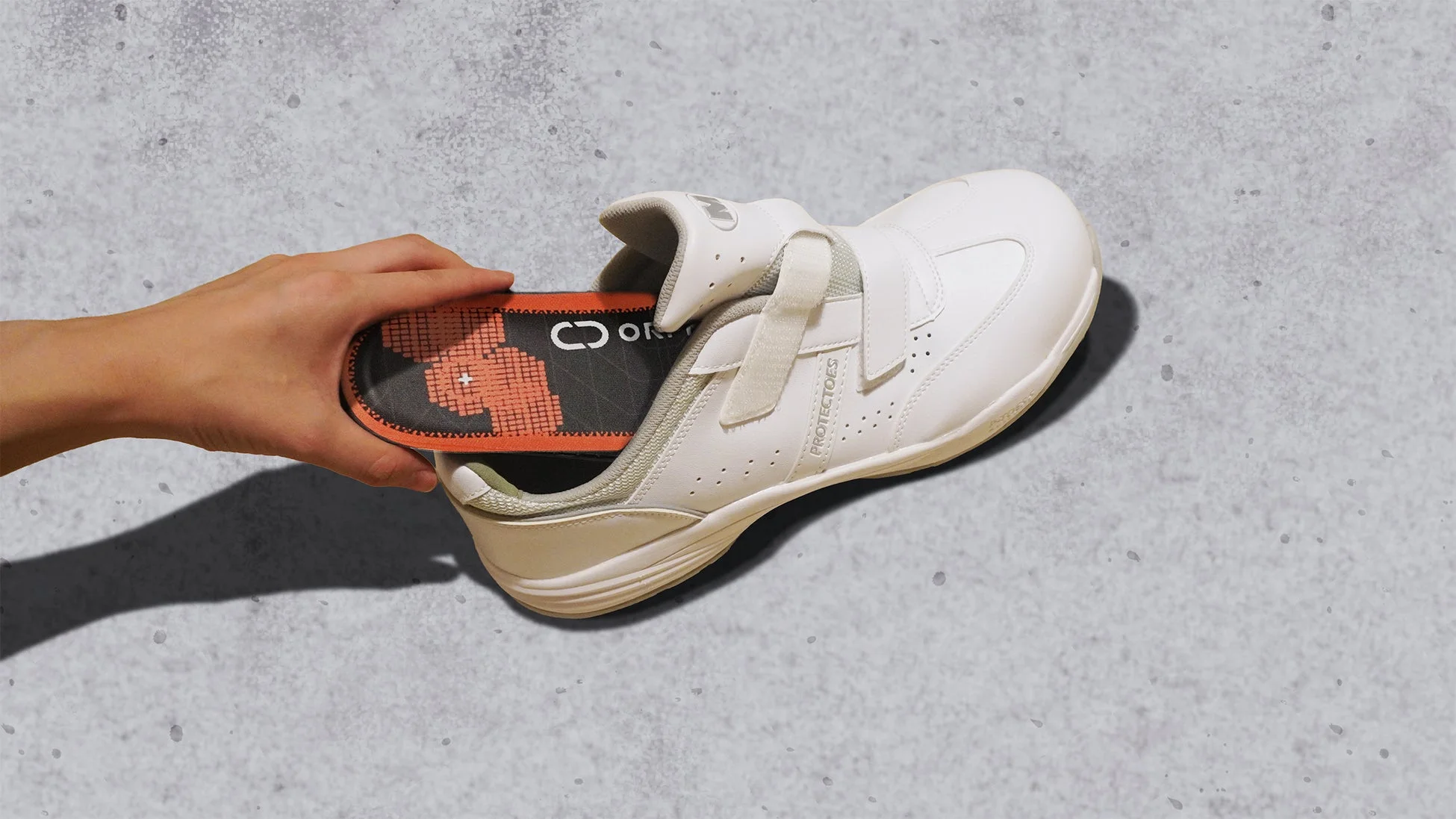 白いベルクロストラップの靴に、手がインソールを差し込んでいる様子