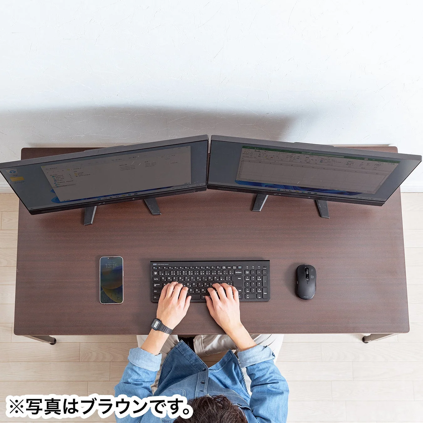 ブラウンのデスクでデュアルモニターを使って作業する人の俯瞰写真