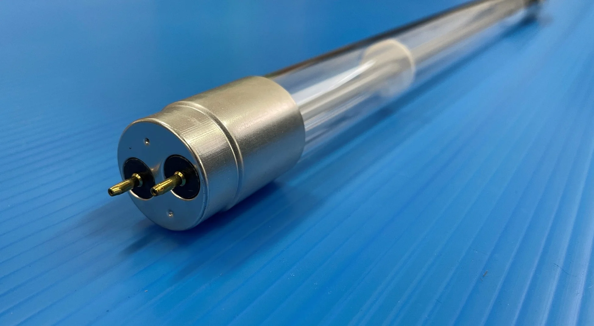 青い背景の上に置かれた、金属製のキャップと2本のピンが付いた透明なガラス管