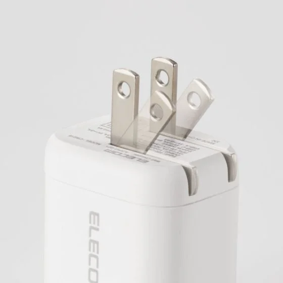 白いELECOM製のACアダプターがクローズアップで写っています。プラグ部分は折りたたみ式で、携帯性に優れていることが特徴です。入力・出力電圧などの仕様が印字されており、スマートフォンなどのデバイス充電に適した製品です。