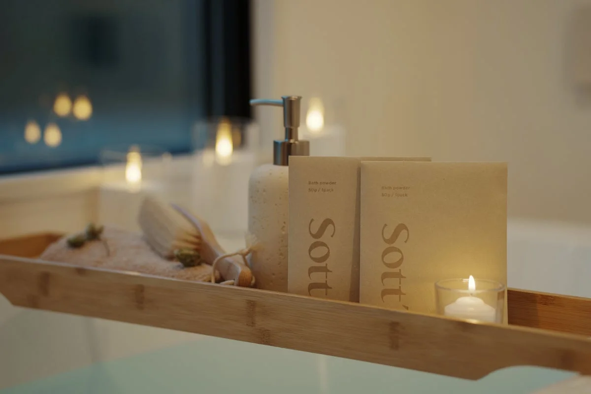 バスタブに渡された木製トレイに、バスパウダー、ポンプボトル、バスブラシ、そして灯されたキャンドルが並べられ、リラックスできるバスタイムを演出している様子。