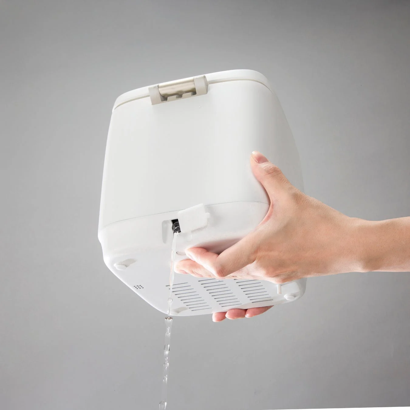 白い家電製品を傾け、底部の開口部から水を排出している様子です。