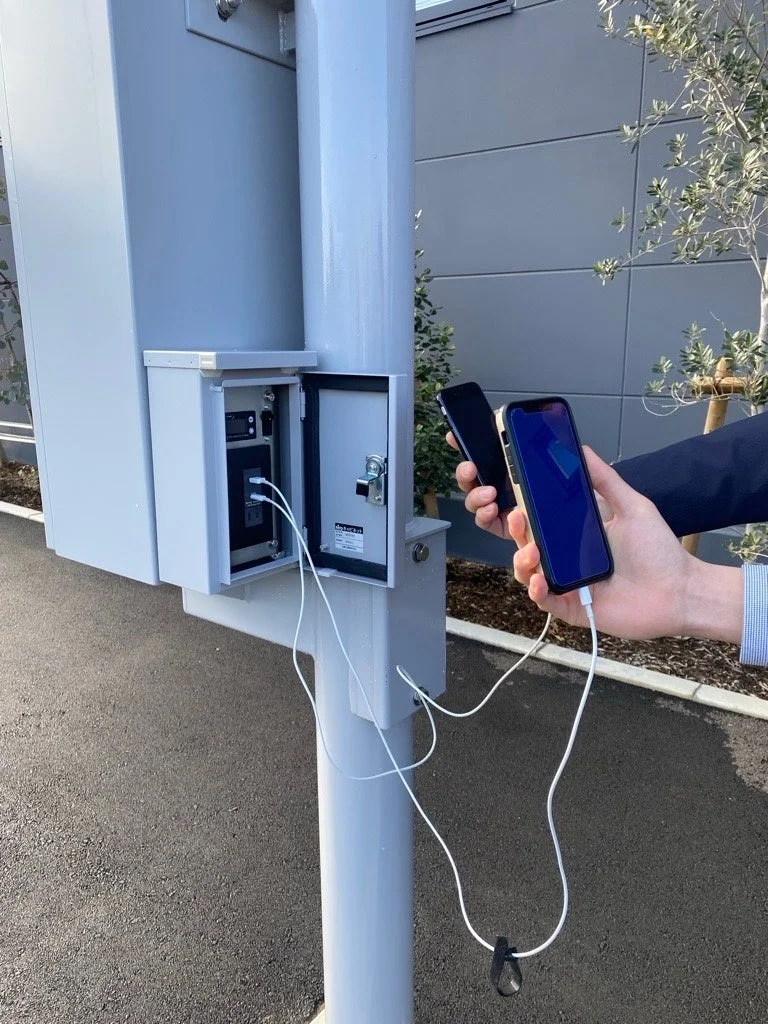 屋外のポールに設置された充電ステーションでスマートフォンを充電している様子