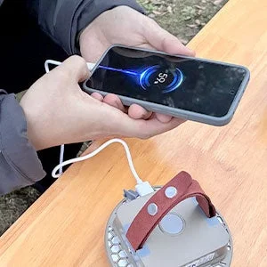 屋外の木製テーブルで、人物がスマートフォンをポータブル電源らしき機器で充電している様子。スマートフォンの画面にはバッテリー残量「59%」が表示されています。