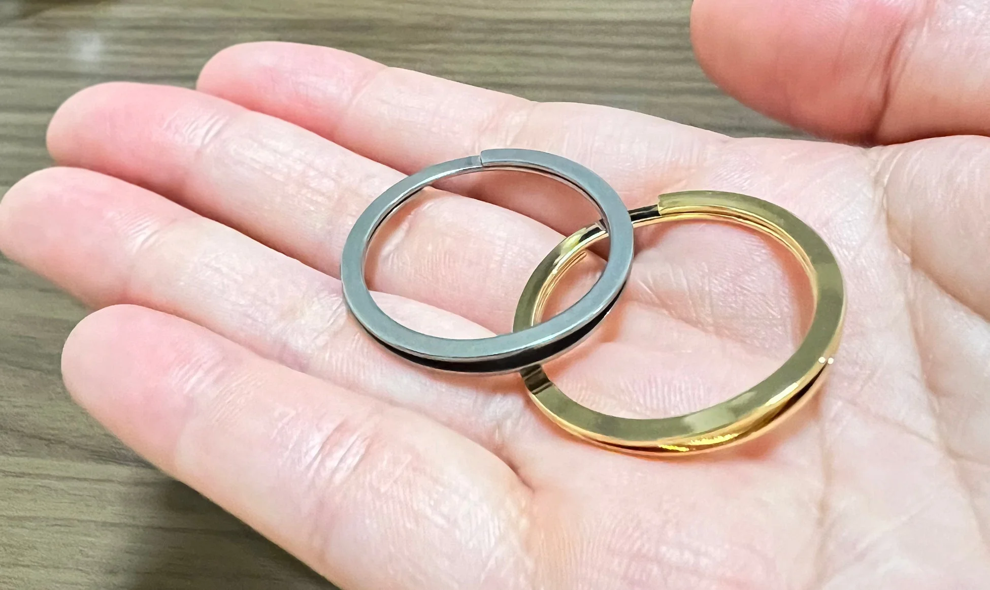 手のひらに置かれた、ゴールドとシルバーの2つの平らな金属製キーリング