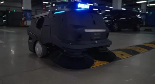 青い光を放つ自動清掃ロボットが、地下駐車場で路面の清掃作業を行っている様子を捉えた画像です。