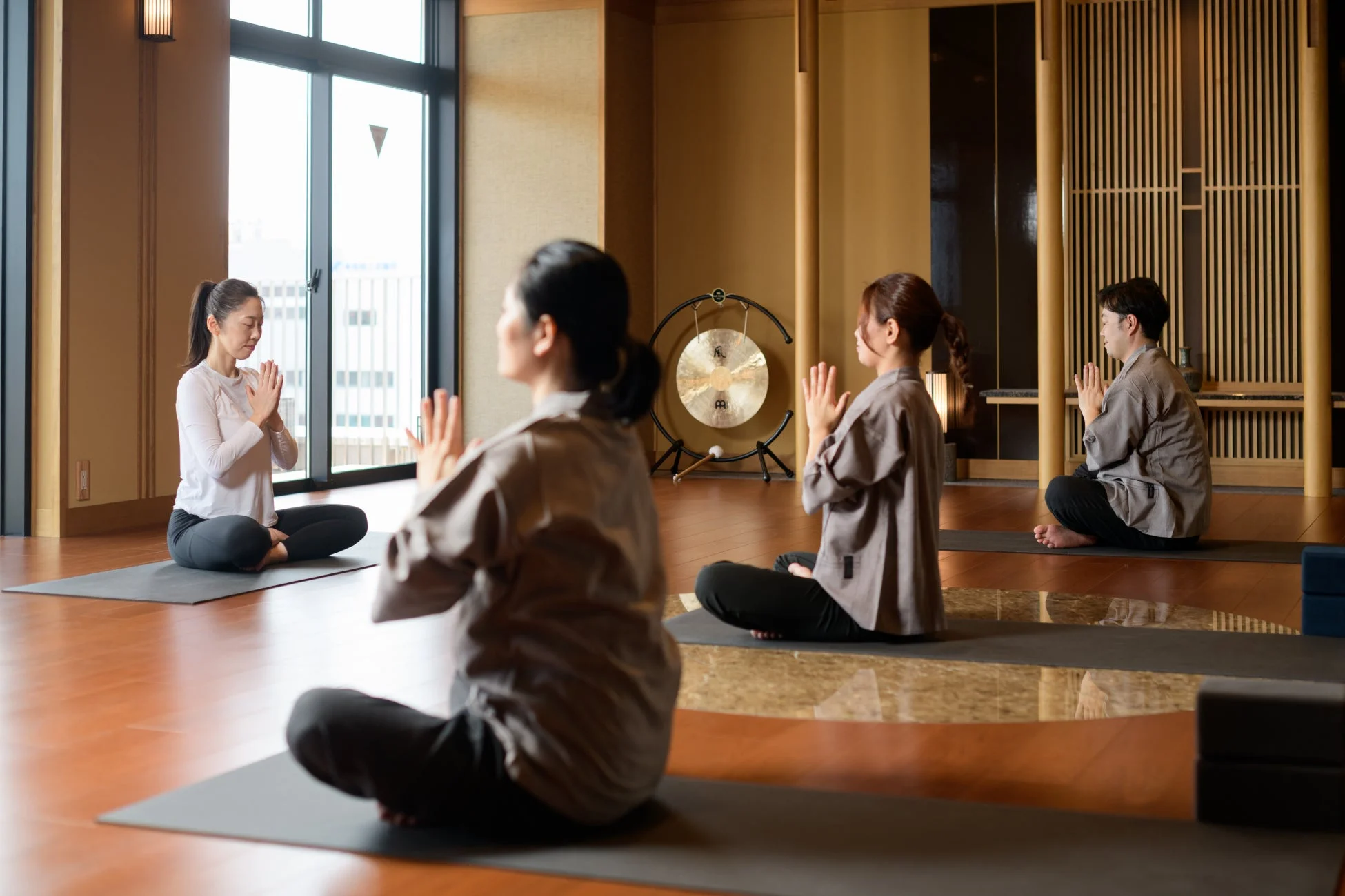 和風の落ち着いたスタジオで、数人の人々がヨガマットの上で瞑想している様子