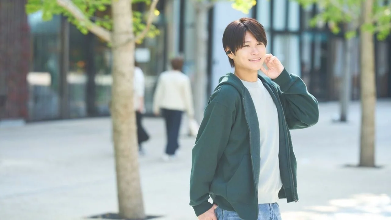 緑色のパーカーを着た男性がイヤホンを装着し、笑顔を見せている画像