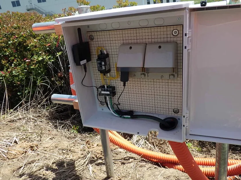 屋外に設置された白い制御ボックスが開いており、内部には配線された電気部品が見える