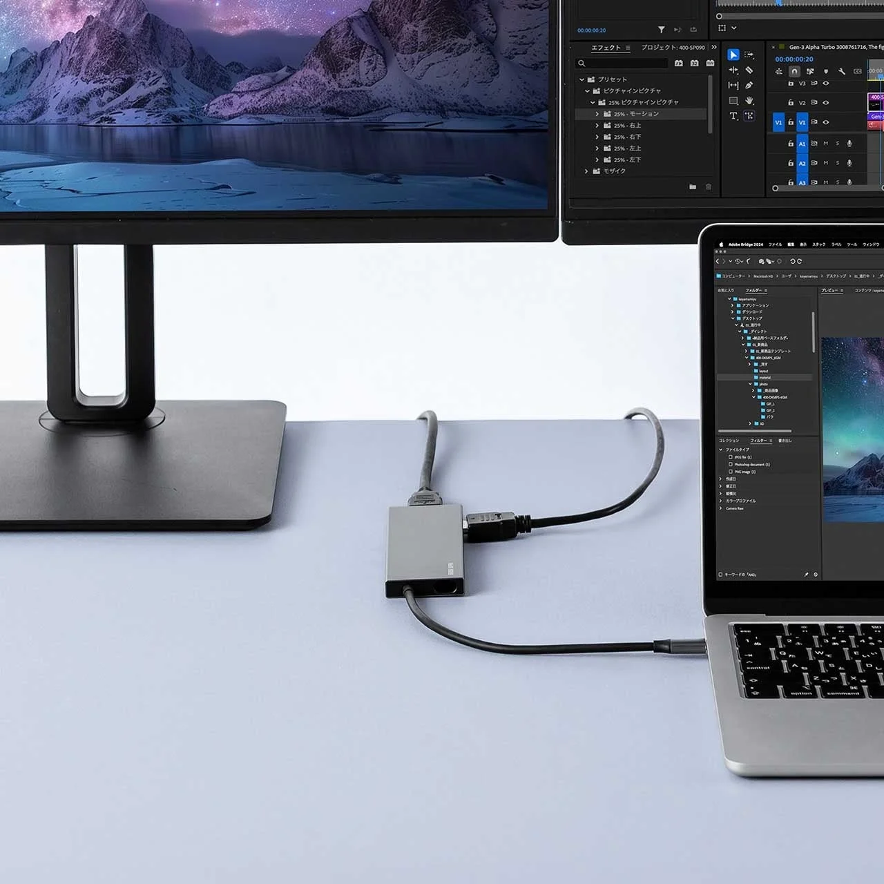 ノートパソコン、ハブ、外部モニターで構成されたデスクワーク環境。MacBookと大型ディスプレイが接続され、映像編集や写真管理の画面が表示されています。Ugreenのハブが使用されています。