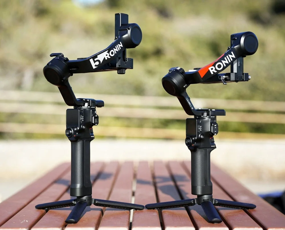 屋外の木製テーブルに置かれた2台の黒いカメラ用ジンバル