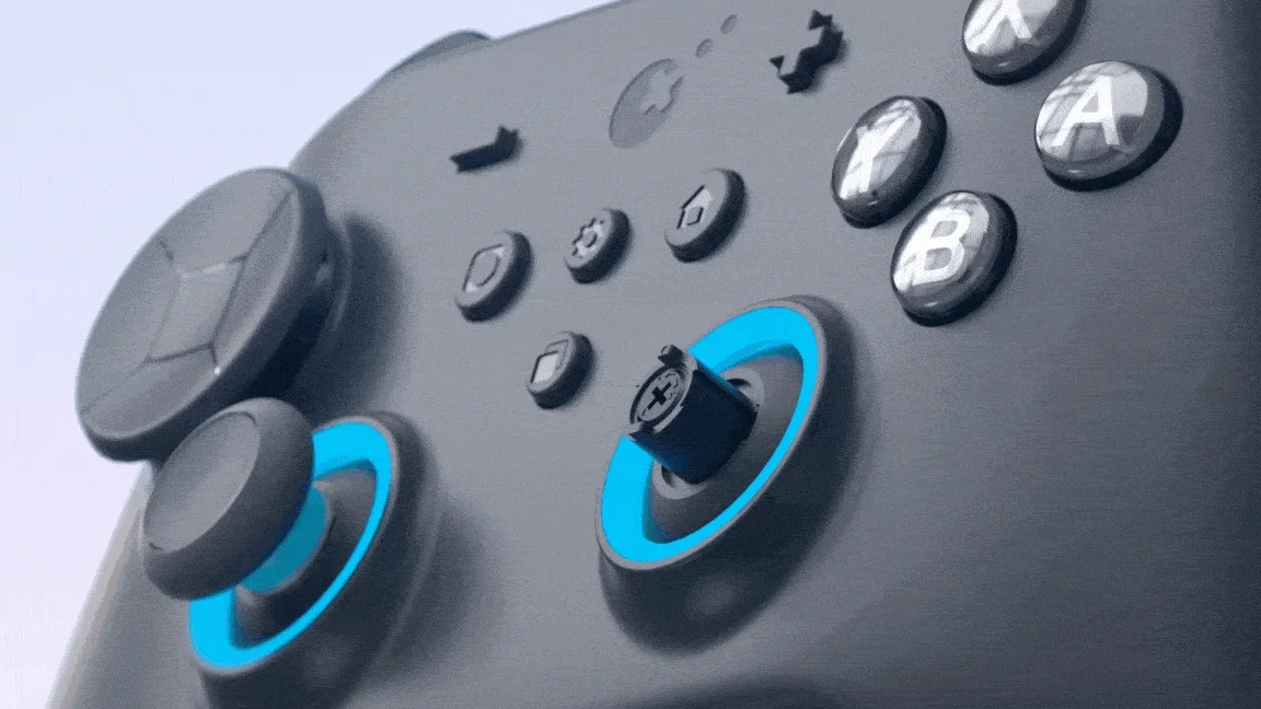 青い光が特徴的な黒いゲームコントローラーのクローズアップです。ジョイスティックやA/B/X/Yボタンが鮮明に写っており、右のジョイスティックは内部構造が見えています。