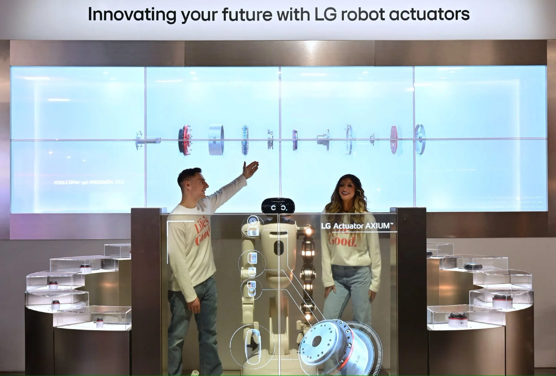 LGのロボットアクチュエーターを展示するイベントの様子。透明なディスプレイにロボットの構造や製品情報が表示され、男女2人が説明を行っている。未来志向の技術革新が強調された展示風景が捉えられている。