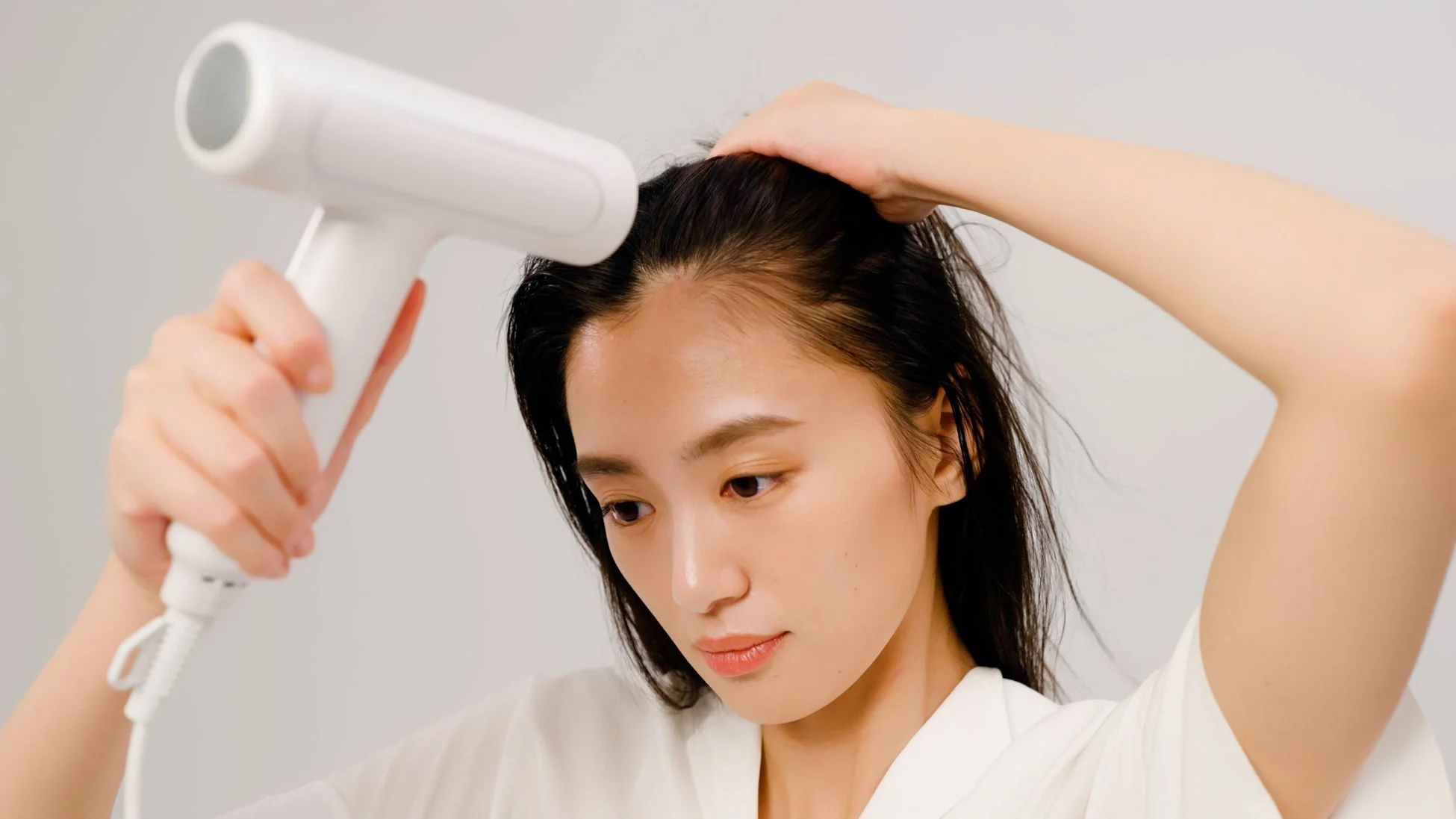 白いヘアドライヤーで髪を乾かす若い女性の様子