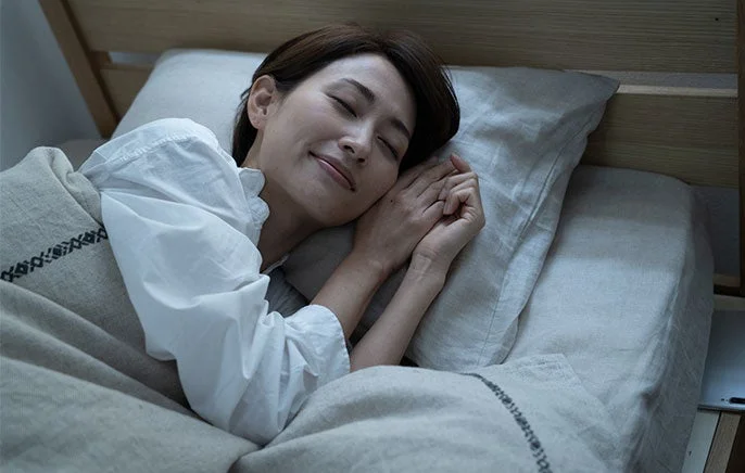 ベッドで安らかな寝顔を見せて眠る女性の姿。穏やかな表情で、心身ともにリラックスしている様子が伝わってきます。