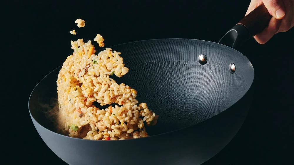 暗い背景の中、熱い中華鍋で炒飯がダイナミックに舞い上がっている瞬間。