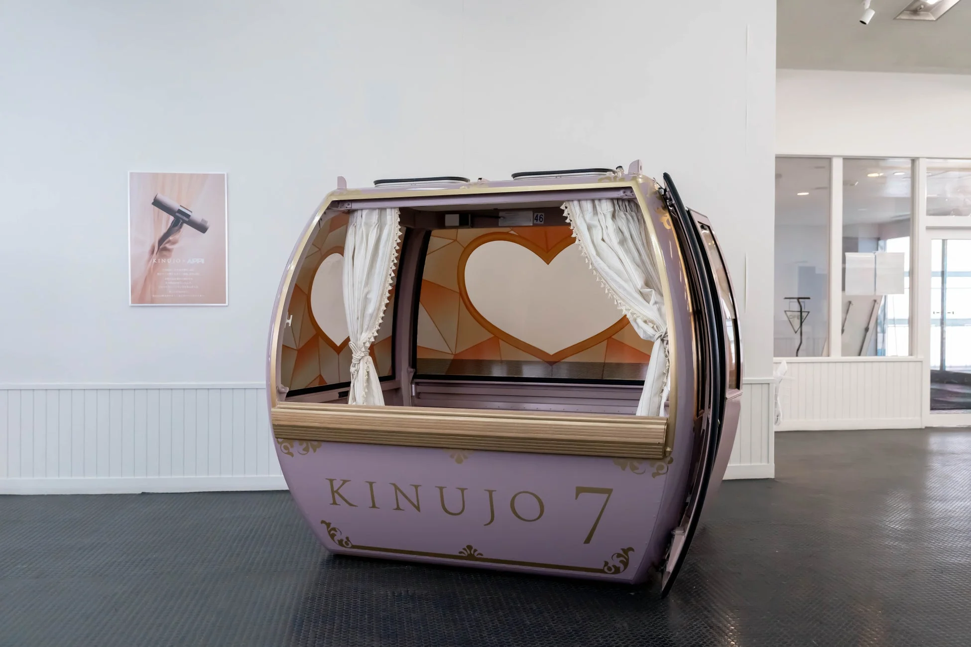 ハートの窓と白いカーテンで飾られたラベンダー色のゴンドラが屋内に展示されている