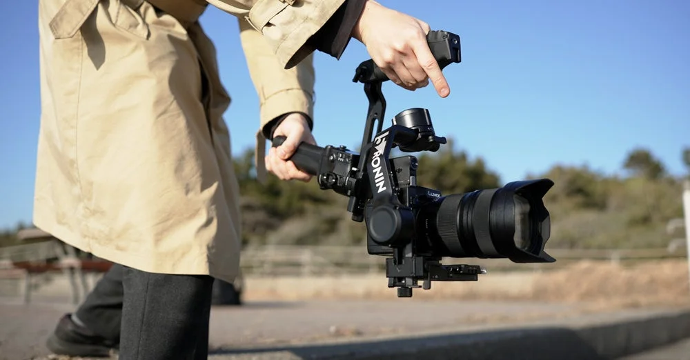 トレンチコートを着た人物が、屋外でカメラとジンバルスタビライザーを操作している様子