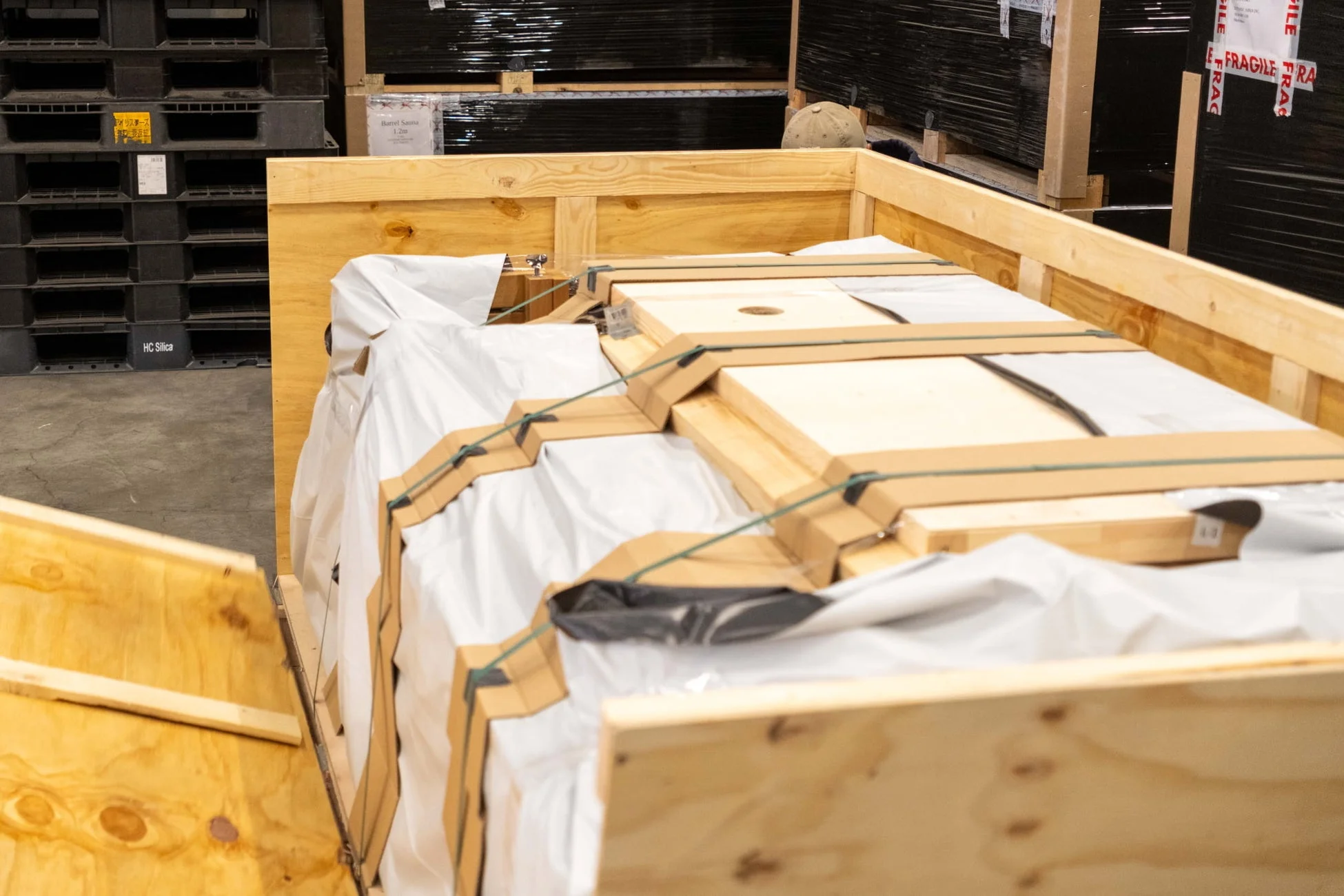 倉庫内で開かれた木箱の中に、白い資材で厳重に梱包され、ストラップで固定された大きな荷物が積載されている様子