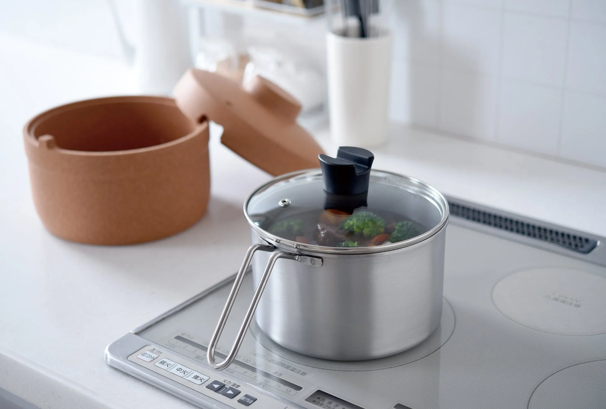 IHクッキングヒーターの上でブロッコリーなどが入った鍋が調理されており、清潔感のあるキッチンで料理をしている様子