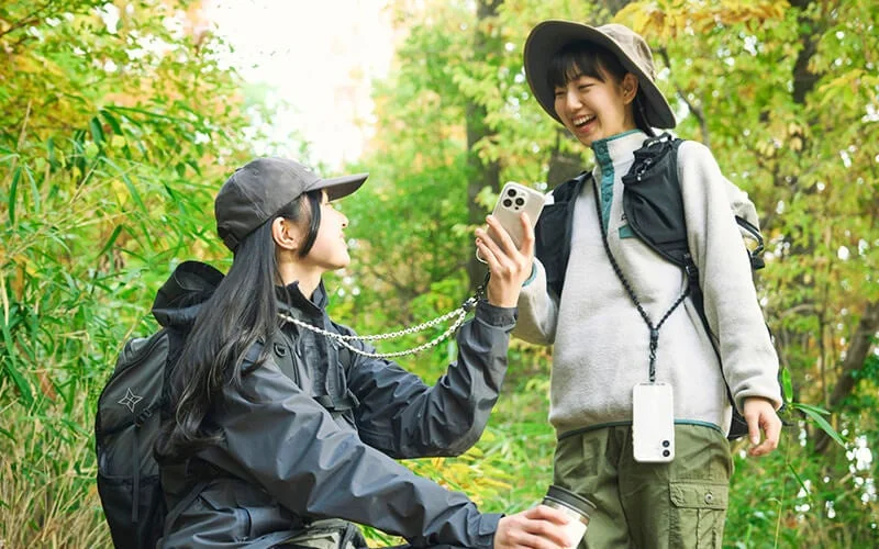 緑豊かな森の中で、アウトドアファッションに身を包んだ2人の若い女性が楽しそうに交流している様子