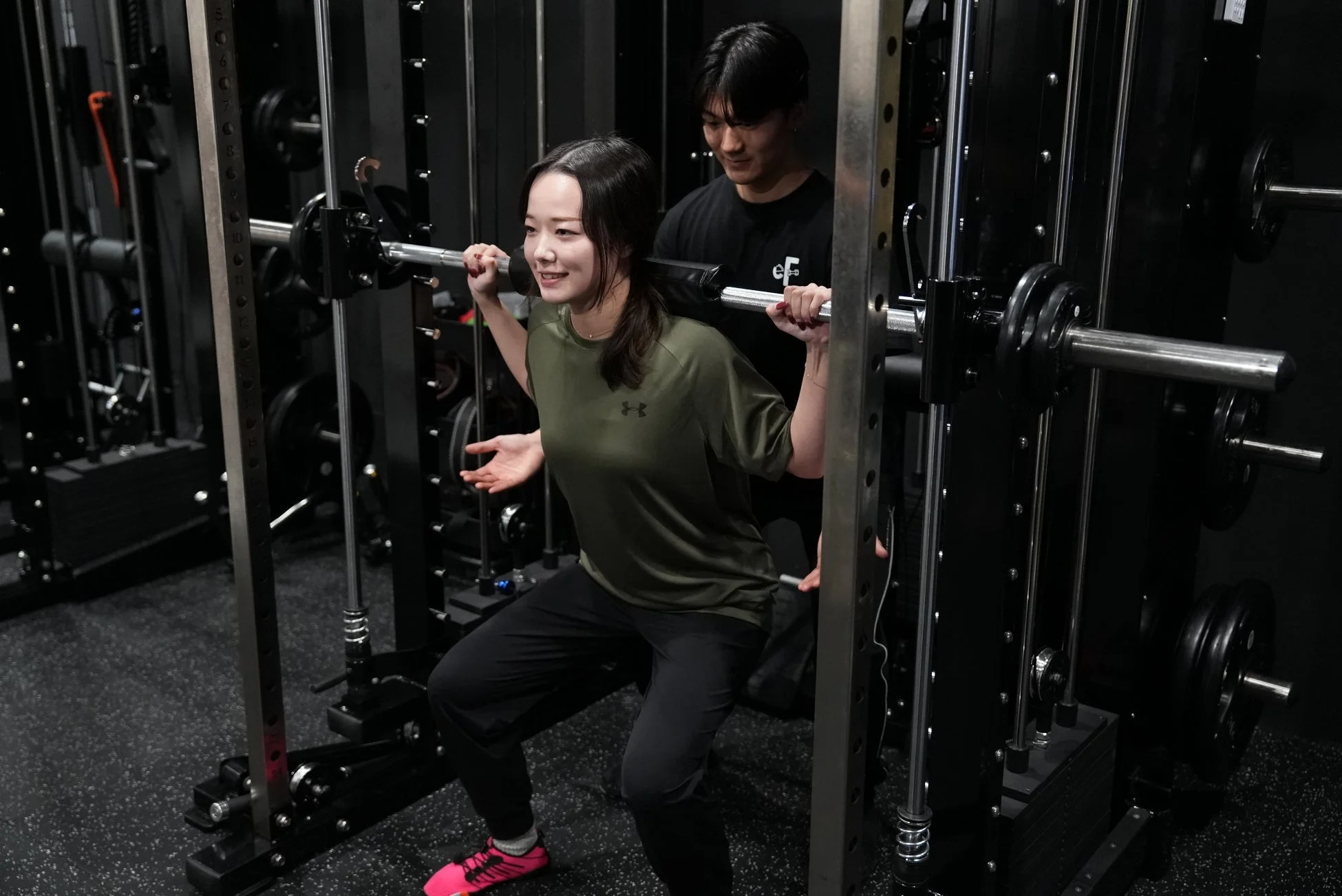 ジムでバーベルスクワットを指導する男性トレーナーと女性