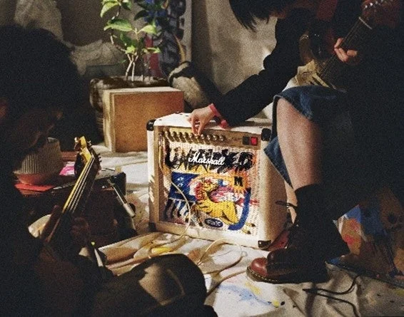 ギターアンプのつまみを調整する人物とギターを弾く人物