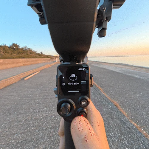 夕焼けの海辺で手持ちのジンバルカメラを操作している様子