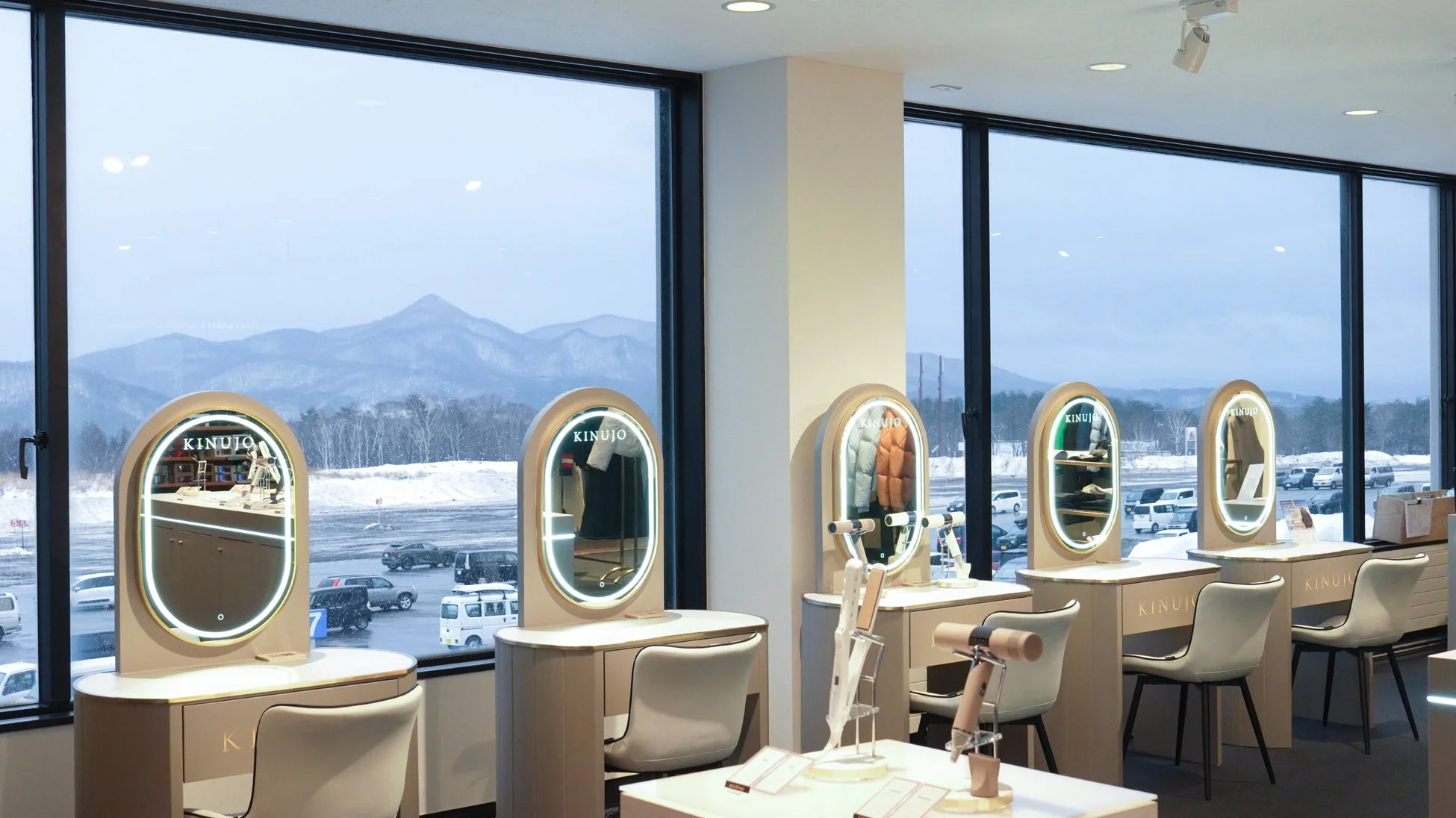 窓の外に雪景色と山々が広がるモダンな店舗の内部。KINUJOのドレッサーと美容家電が並ぶ